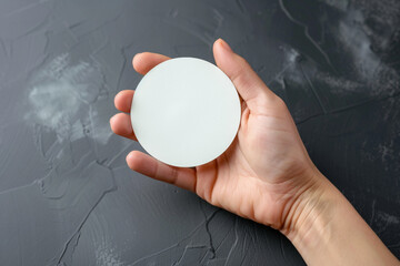 Hand holding round blank white sticker mock up isolated on gray. Sticker mockup holder. Empty paper clue remnder hold in hands. Arm sticking round sticker.