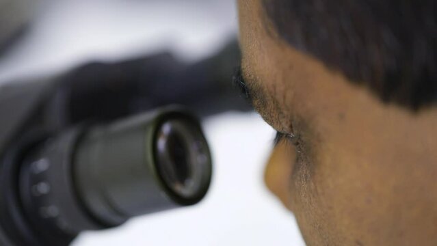 asian man looking into a microscope lens close up for microscopic metal structure checking analysis in process quality checks and control in a science laboratory. scientific study diversity