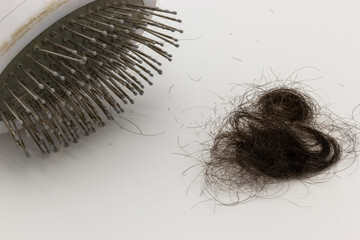 Hair brush next to a pile of brown hair on a white background. This image can be used to illustrate...