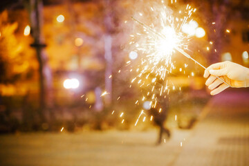 Woman holding sparkler night while celebrating Christmas outside. Dressed in a fur coat and a red...
