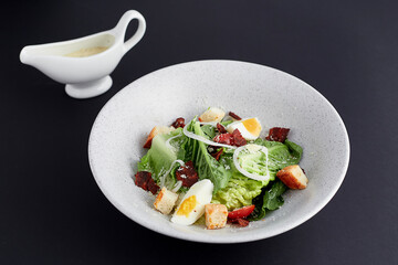 Boiled egg and ham with green cos lettuce salad topped with sliced onions, croutons and cheese served in a white bowl with cream salad (dipping sauce) isolated on black background. Clean food.