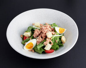 Boiled egg and tuna with green cos lettuce salad topped with sliced onions, tomato and croutons served in bowl isolated on black background. Clean food.