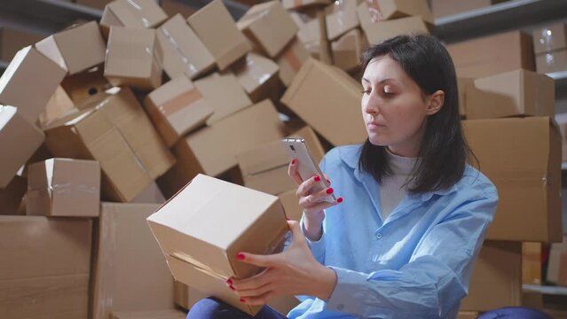 A young female worker scans boxes in a small warehouse close up