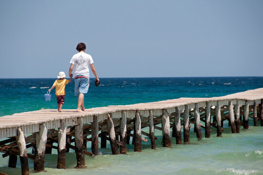 Alcudia, Playa de Muro, Muro beach, Majorca, Mallorca, Spain, Europe - young father and little son walking hand in hand on wooden planks pier at the seaside, Muro beach