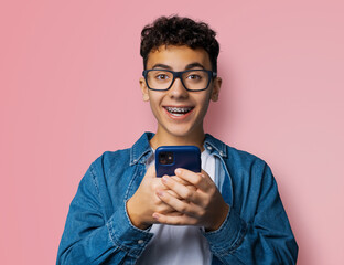 Excited surprised shocked astonished happy black curly haired funny young man wear braces eye glasses spectacles open mouth hold typing cell phone cellular smartphone cellphone isolated background.