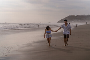 Couple in love laughing and walking hand in hand on the shore of the beach