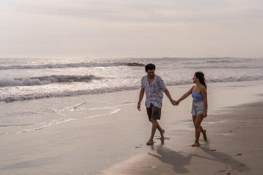 Lovers laughing and walking hand in hand along the beach