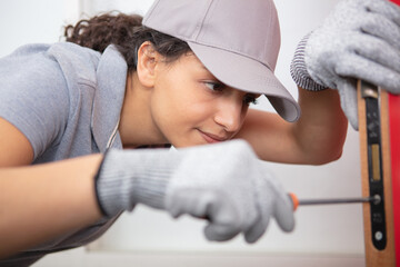 happy female builder using a screwdriver on a door