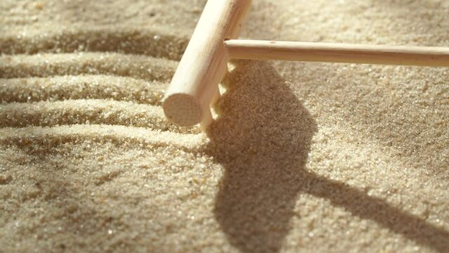 Close-up making zen garden with sand and stone using mini bamboo wooden rake