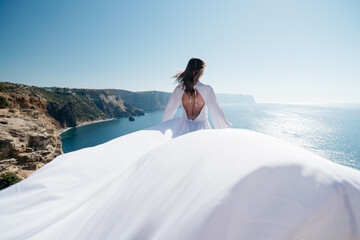 A woman in a white dress is standing on a cliff overlooking the ocean. The scene is serene and peaceful, with the woman's dress flowing in the wind. The ocean in the background is calm and inviting.