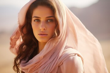 
A candid shot of a young Bedouin woman, her veil gently fluttering in the desert breeze, showcasing the delicate intricacies of her pastel-hued garments