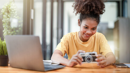 Curious young woman exploring a vintage film camera at a well-lit indoor workspace with technology...