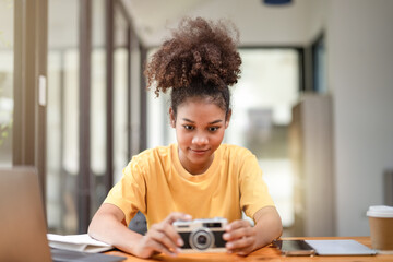 Curious young woman exploring a vintage film camera at a well-lit indoor workspace with technology around.