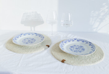 Elegant table setting with two wineglasses and beautiful plates on wicker cream table-napkin....