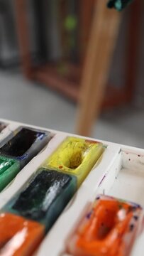 Set of multicolored watercolor paints and white ceramic palette close up in art studio. Artist's tools and colors on vertical video
