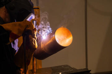 A man wearing a protective mask welds a metal pipe. 