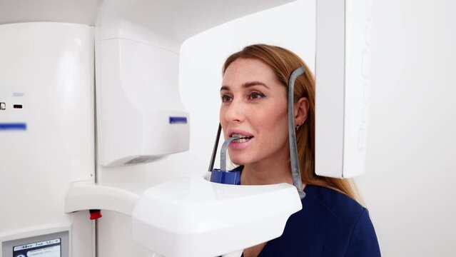 Female patient at panoramic x-ray shot of jaw holding face at x-ray machine. Woman standing in dental x-ray unit laser precise projection for dental radiography. Examining teeth in the modern clinic.