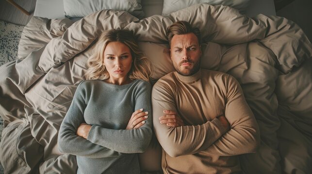 Young Couple Lying In Bed, Upset, Facing Away From Each Other.