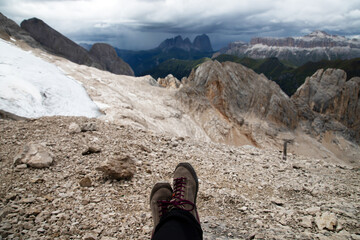 Trekking boots of a hiker while sitting on top of a mountain in Dolomites, Italy - 775640565