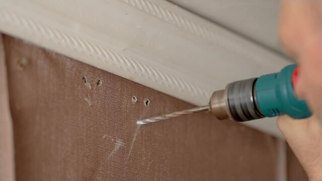 Close up man drills wall to hang cornice and makes hole. Bad flimsy walls in old apartment. Slow motion video of man using drill to make hole in wall