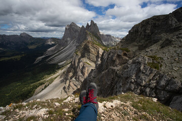 Trekking boots of a hiker while sitting on top of a mountain in Seceda, Dolomites, Italy - 775641591