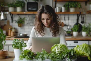 Obraz na płótnie Canvas Young Woman Sits With A Laptop At A Table In The Kitchen Surrounded By Greens And Vegetables. Concept Lchf Diet