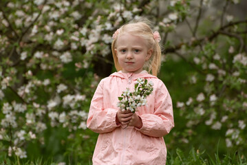 Portrait of serious little caucasian girl with spring floral garden in sunny day with flowering branch