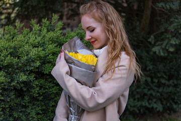 Happy young woman holding bouquet of yellow tulips. Smiling girl with flowers in park waiting for someone. First dating