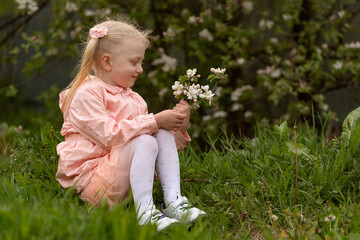 Smiling little lady in pink dress in the garden. Girl sitting with blooming branch and looking on their