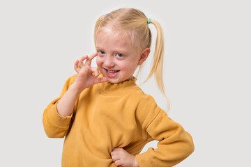 Portrait of a cute little girl in a yellow sweater showing ok sign with fingers