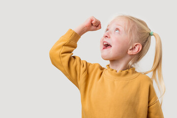 Cute little girl in yellow pullover screaming and looking up on grey background