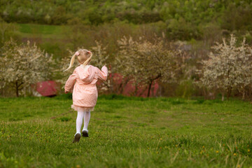 Girl in pink jacket runs through clearing. Child runs and jumping around the field and has fun. Kid rejoices in spring. Springtime.