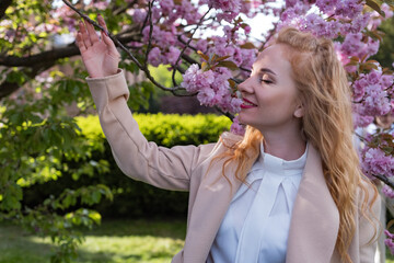 Happy young woman with closed eyes near flowering tree . Portrait of charming fashionable girl in blooming sakura park.
