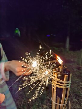Children playing with Bunga Api or Sparkler near oil lamp or lantern. Contains noise and grain due to low light exposure.