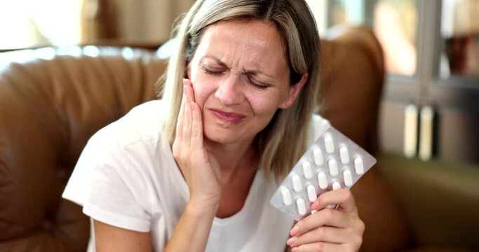 Portrait of woman hurting tooth and taking painkillers pills. Acute toothache and urgent treatment