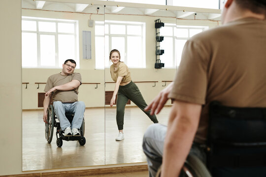 Selective focus shot of man in wheelchair looking into mirror learning dance moves with young female trainer