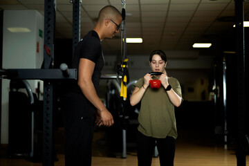 Trainer advises woman during kettlebell exercise in a well-equipped fitness center.