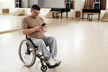 High angle view of mature man in wheelchair scrolling social media page on smartphone during break...