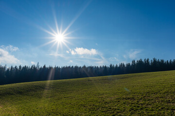 The bright sun behind a forest and a green field