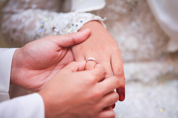 Groom put a ring on finger of his lovely wife. Close up image and selective focus.