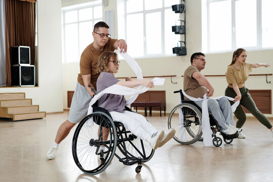 Group of four diverse men and women practicing dance with wheelchairs in studio, long shot