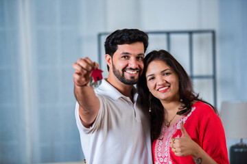 Happy smiling young Indian couple hugging in new home among boxes and showing house keys.