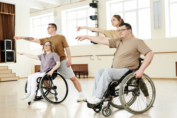 Fototapeta na wymiar Group of four diverse active men and women practicing dance with wheelchairs in spacious studio, long shot