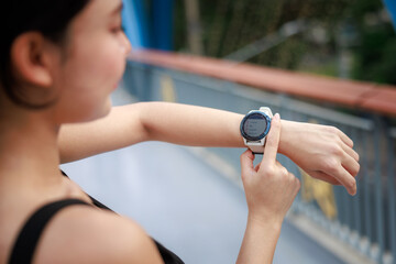 young woman looking down at the timer on her wrist to time before jogging in the morning.