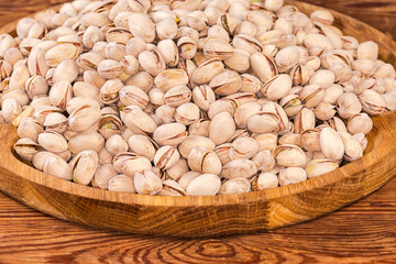 Roasted pistachio nuts on wooden dish, fragment close-up