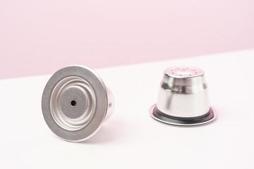 Metal reusable capsules for a coffee machine on a pink and white background close-up.