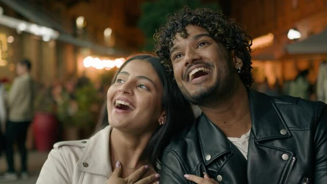 Happy laughing smiling Indian boyfriend man and Arabian girlfriend woman couple travelers tourists in new city contemplate strolling walking cuddling walk at evening night street architecture explore