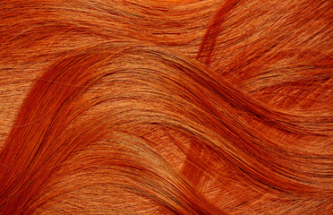 Red hair close-up as a background. Women's long orange hair. Beautifully styled wavy shiny curls. Hair coloring bright shades. Hairdressing procedures, extension.