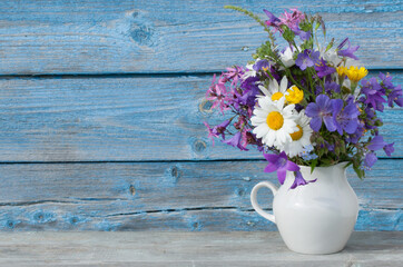 Bouquet of wildflowers in a white jug on a background of a blue wooden wall