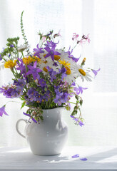 Bouquet of wildflowers in a white jug by the window